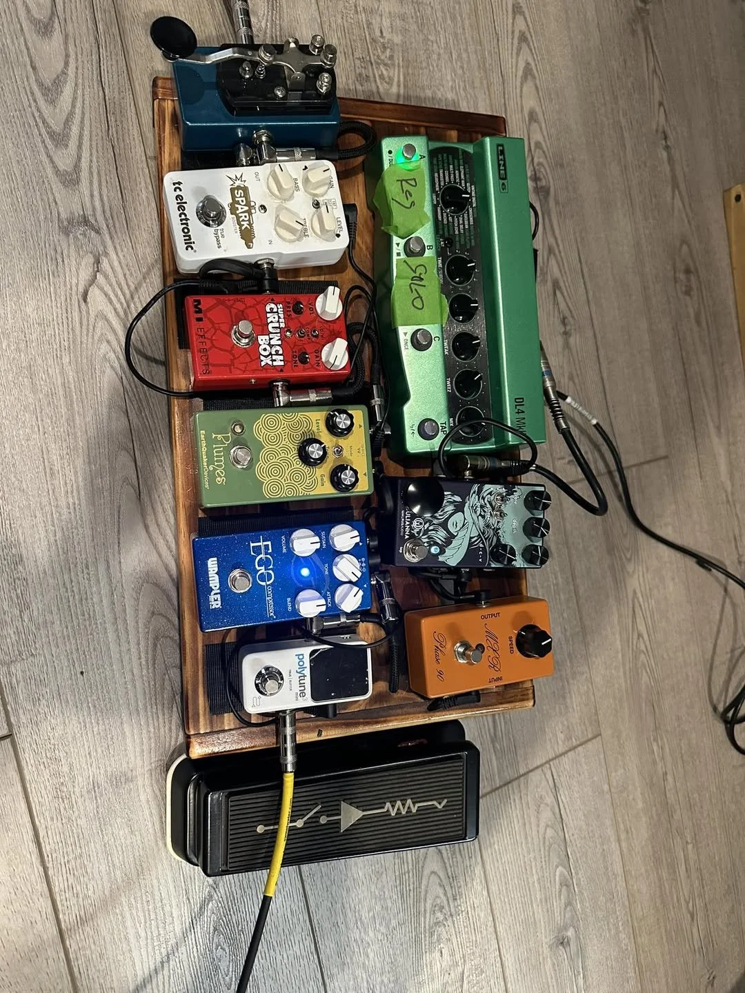 A wooden pedalboard with multiple guitar effect pedals connected with cables, including brands like Boss, Strymon, and Walrus Audio, set on a wooden floor.
