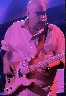 Man playing bass guitar on stage under purple lighting.