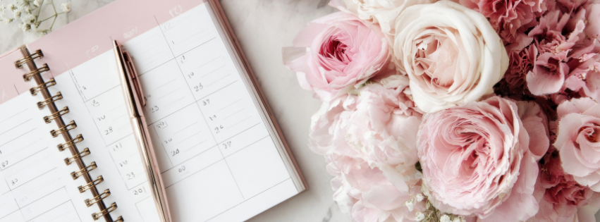 Open weekly planner with a pen next to a bouquet of pink and white roses.
