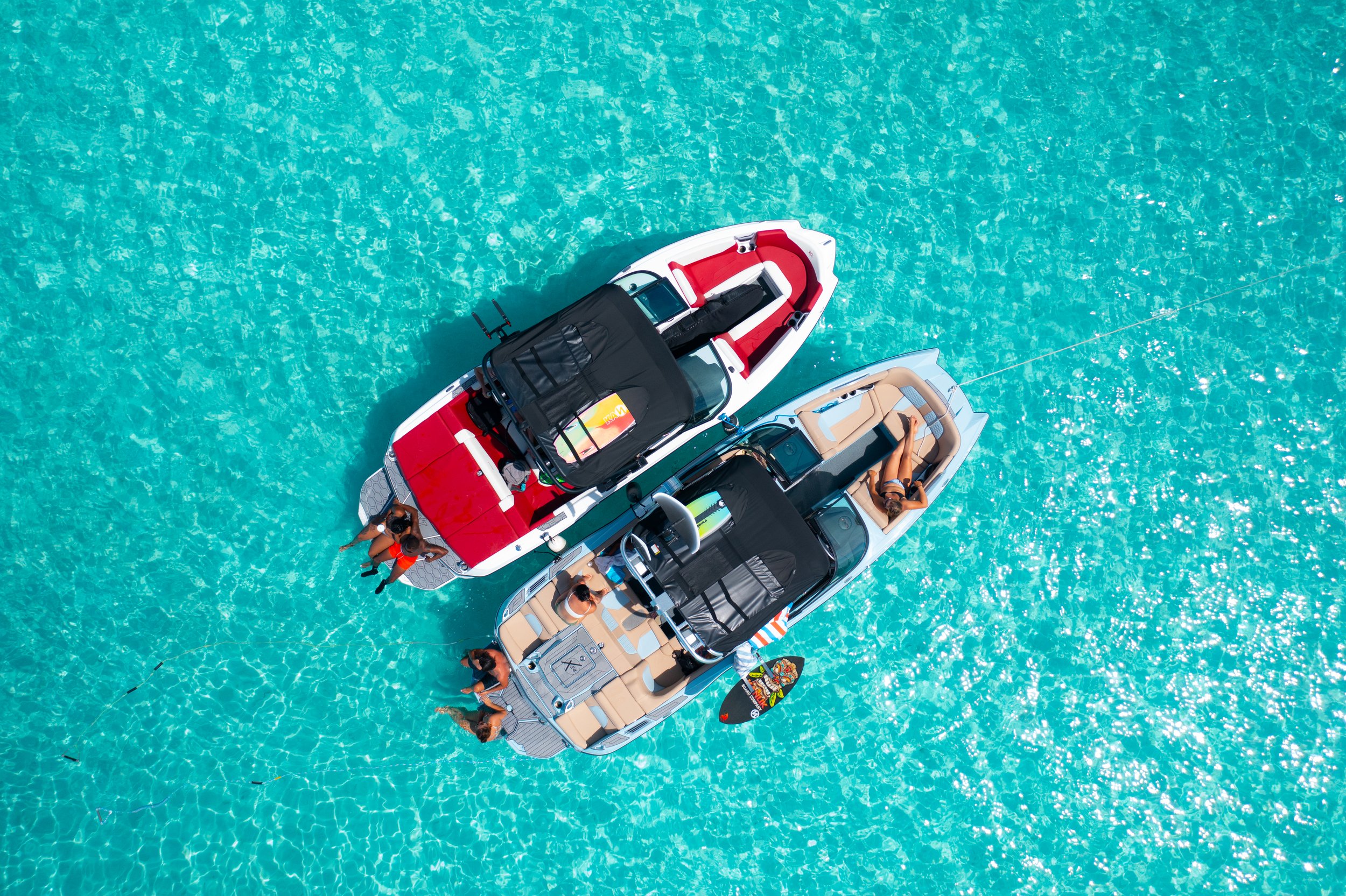 Two wake boats anchored in clear, turquoise water, with people relaxing and enjoying the sunny weather. Perfect for wakesurfing, wakeboarding, waterskiing, tubing. Located in Gracebay, Providenciales, Turks & Caicos.