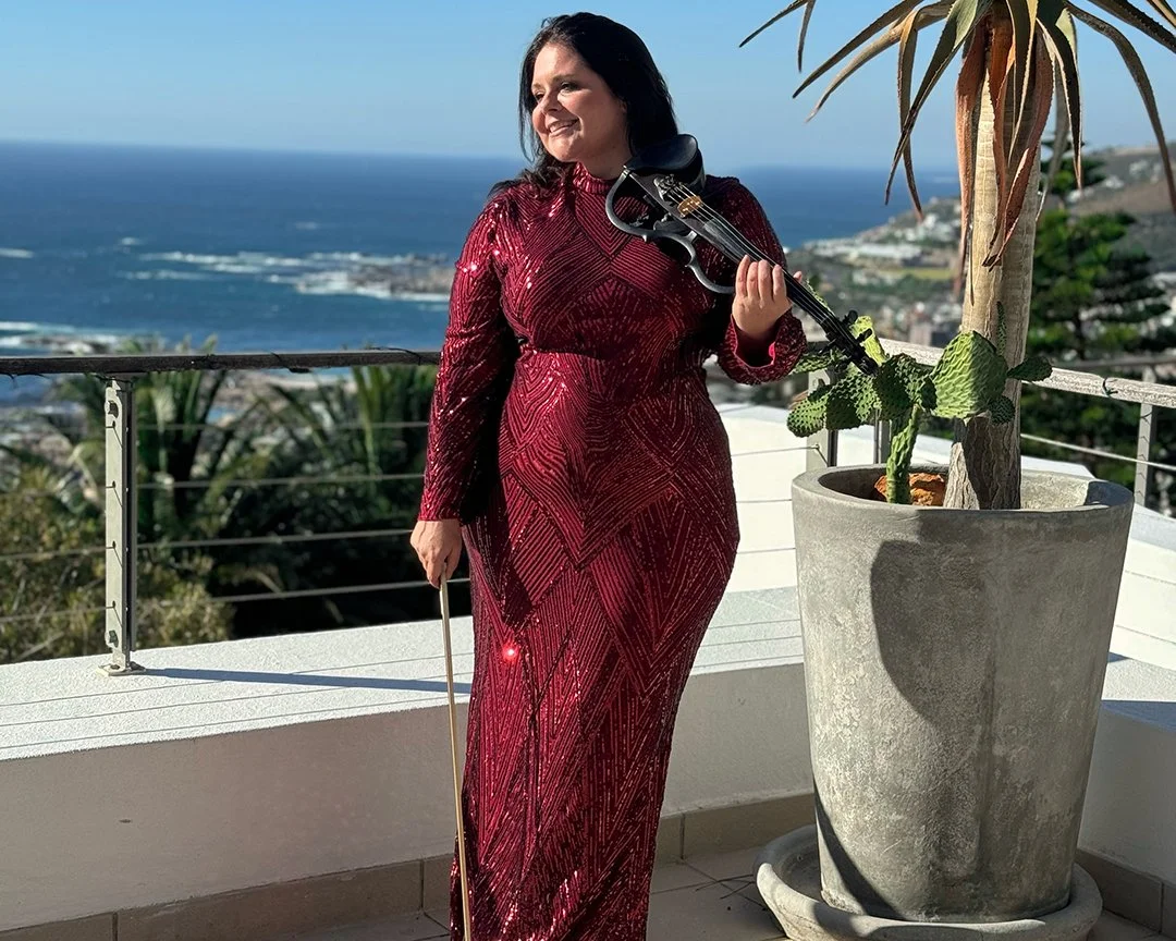 A woman in a sparkling red dress holding aLarah Eksteen performing live violin music at a private birthday celebration in Camps Bay.