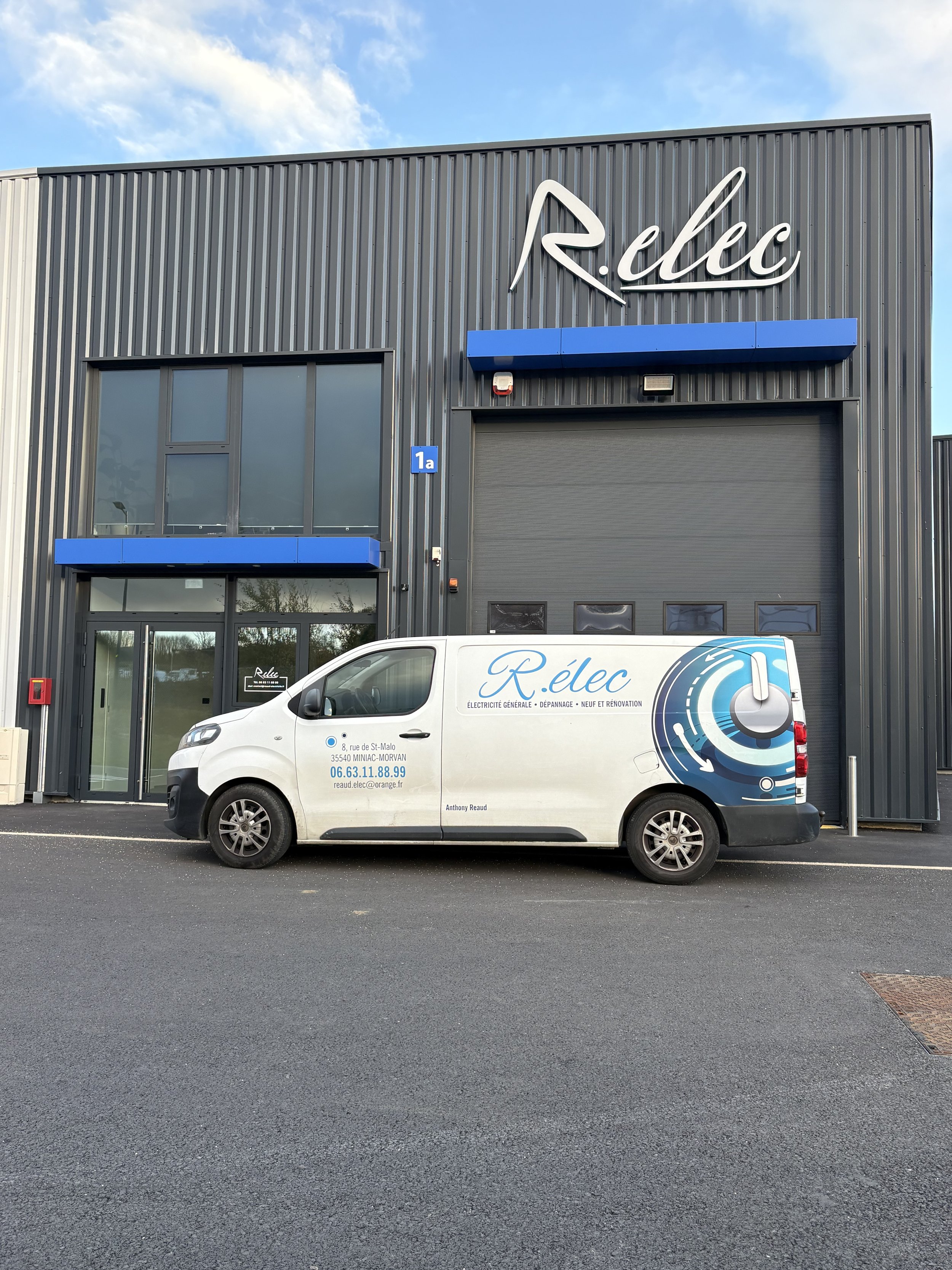 Un bâtiment industriel gris avec une enseigne 'Relec' et une camionnette blanche avec le logo 'Relec' et des informations de contact, stationnés devant l'entrée.