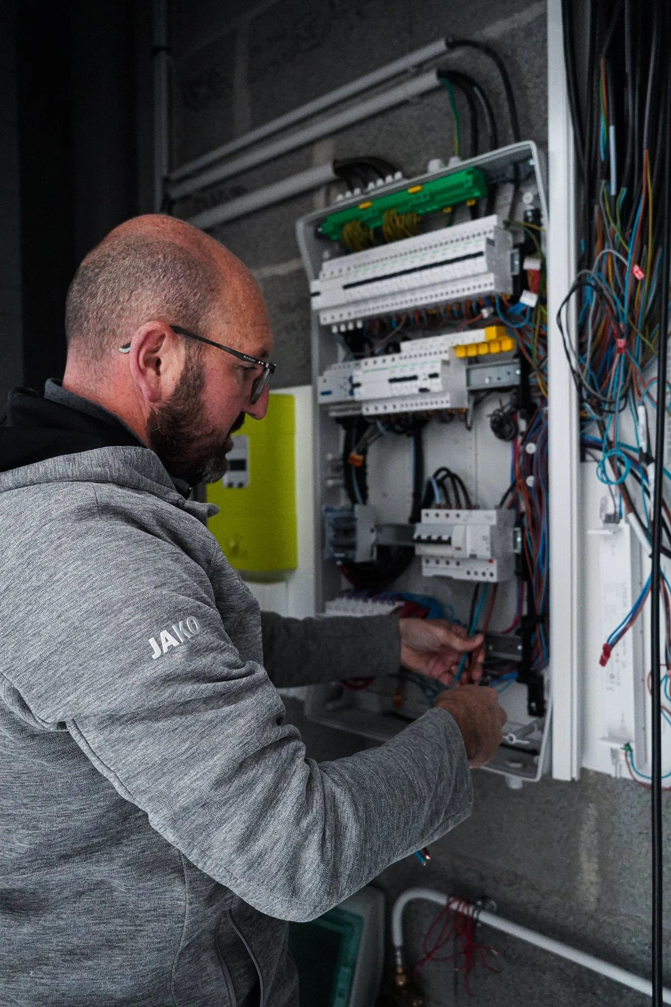 Homme travaillant sur une armoire électrique contenant de nombreux câbles et composants électriques.