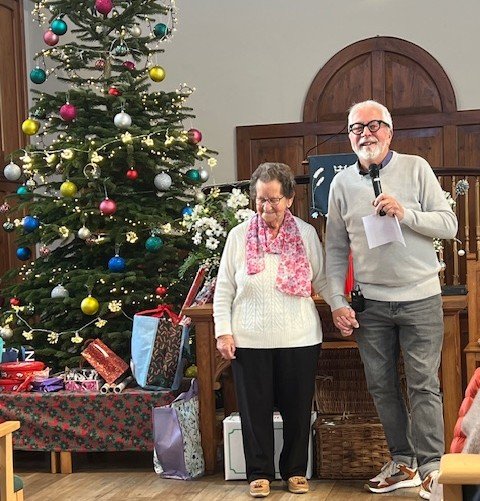 two people with presents beside Christmas tree
