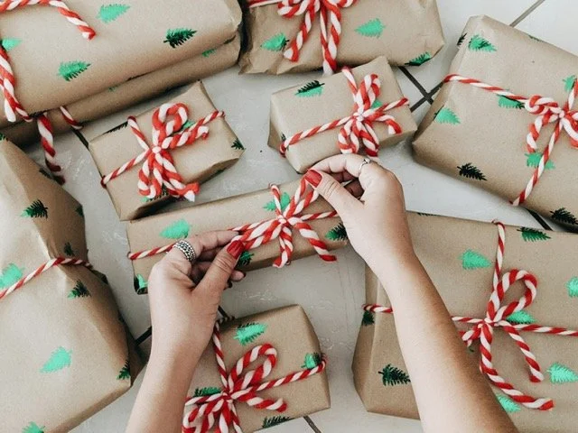 Multiple Christmas presents wrapped in brown paper with green trees, tied with red and white striped ribbons, on a white surface.