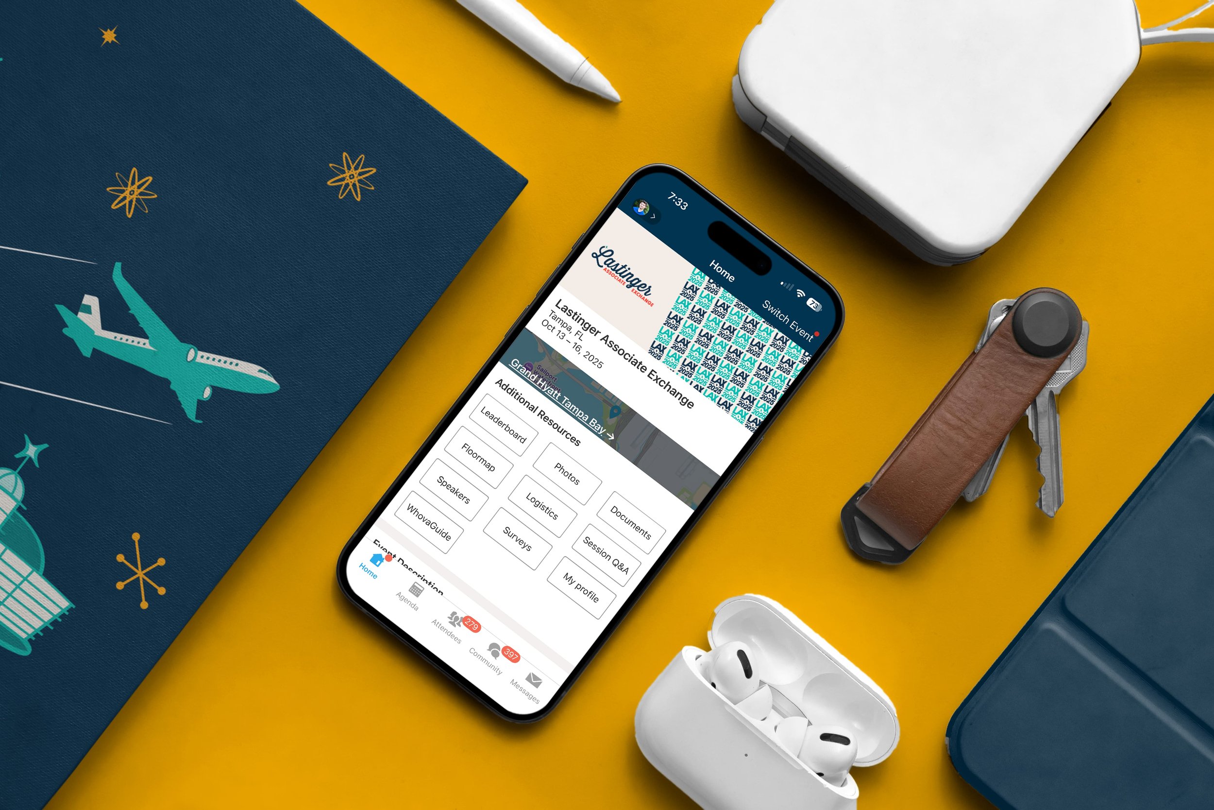 Smartphone displaying event information for Lastinger Associate Exchange on a yellow desk, surrounded by a ray of other travel-related items including wireless earbuds in a white case, a blue suitcase, a leather armrest, a white pen, a white portable charger, a blue notebook with a plane illustration, and keys.