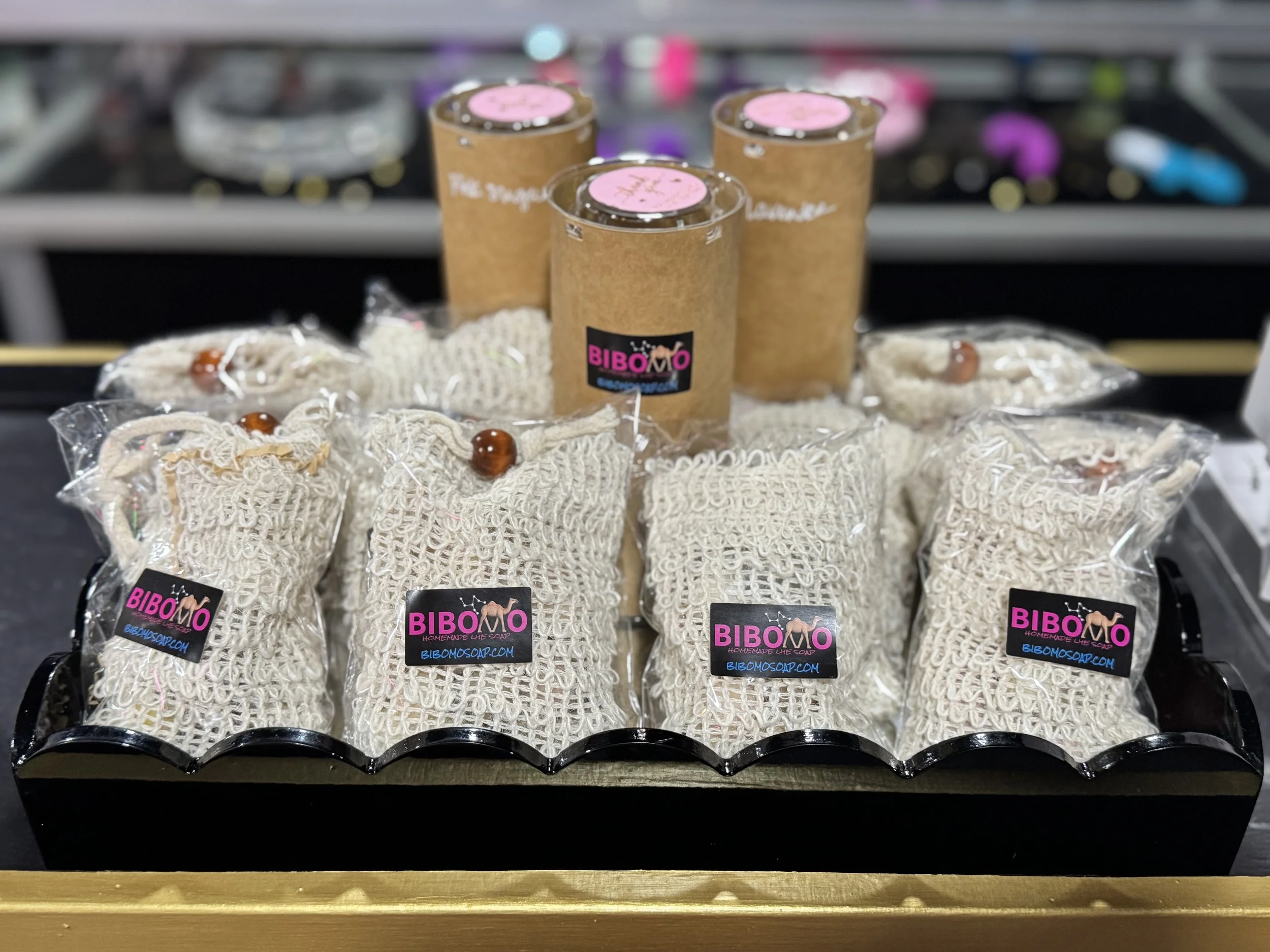Set of handmade soap bars with labels that say 'BIBOMO' and small rolled soap in mesh bags, placed on a tray with some cardboard tubes in the background.