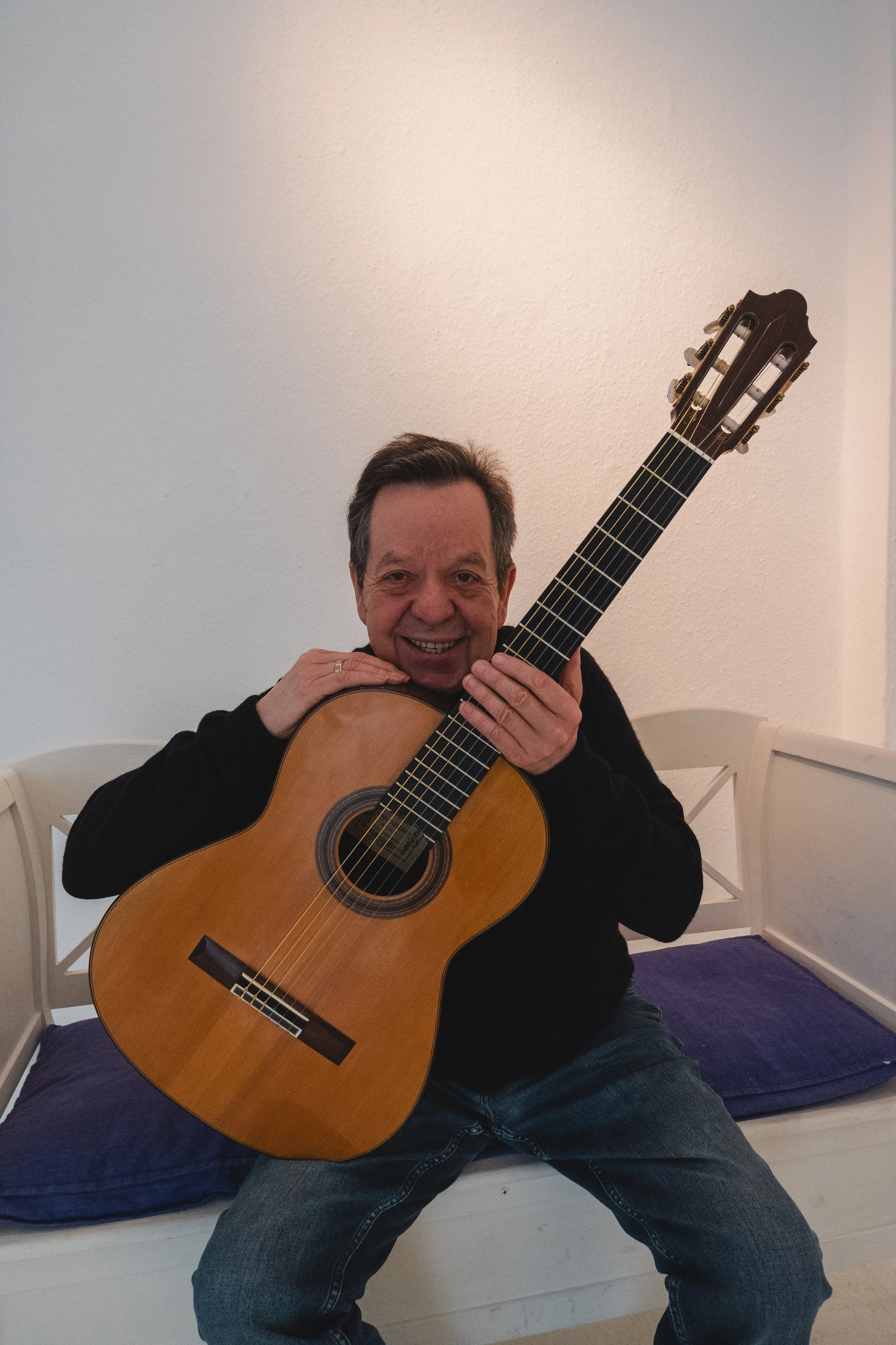Joachim Schrader im Portrait mit einer Gitarre lächelt in die Kamera.