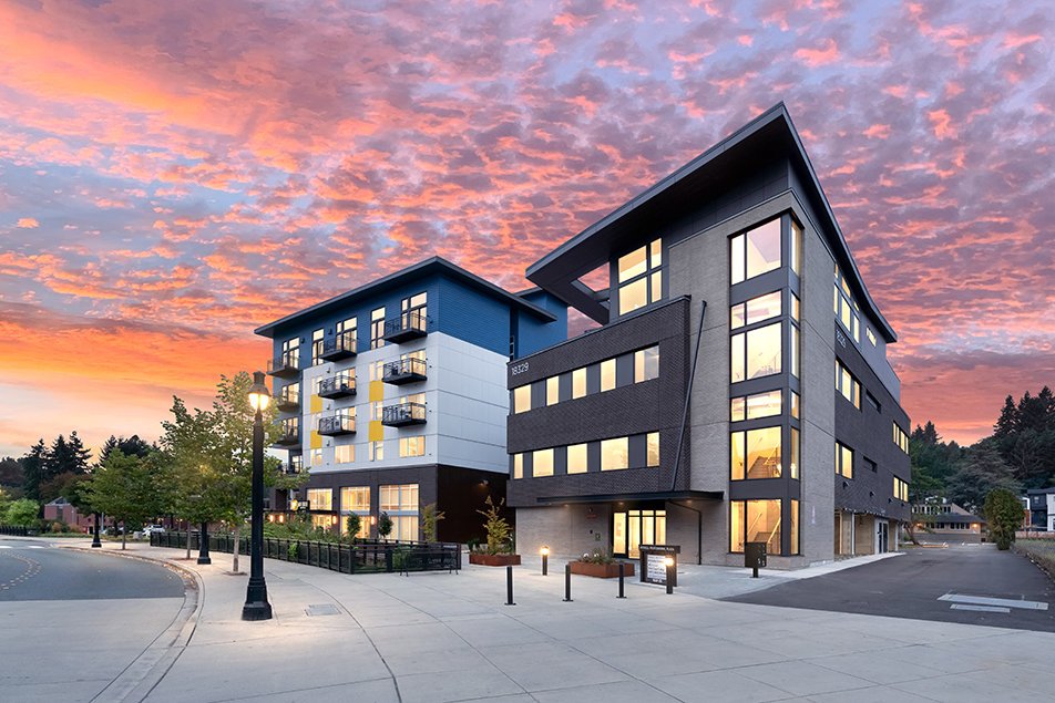 Street-facing view at dusk, showing the adjacent mixed-use building and pedestrian walkway.