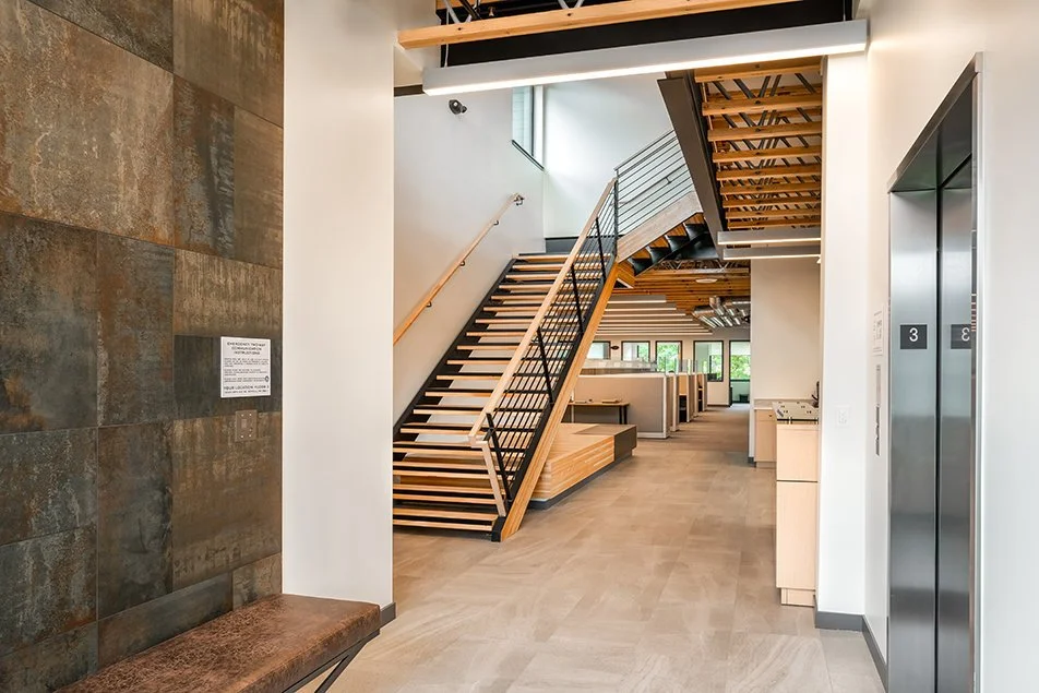 Interior view of the stairwell, showing wood treads, steel railings, and the upper landing with large windows.
