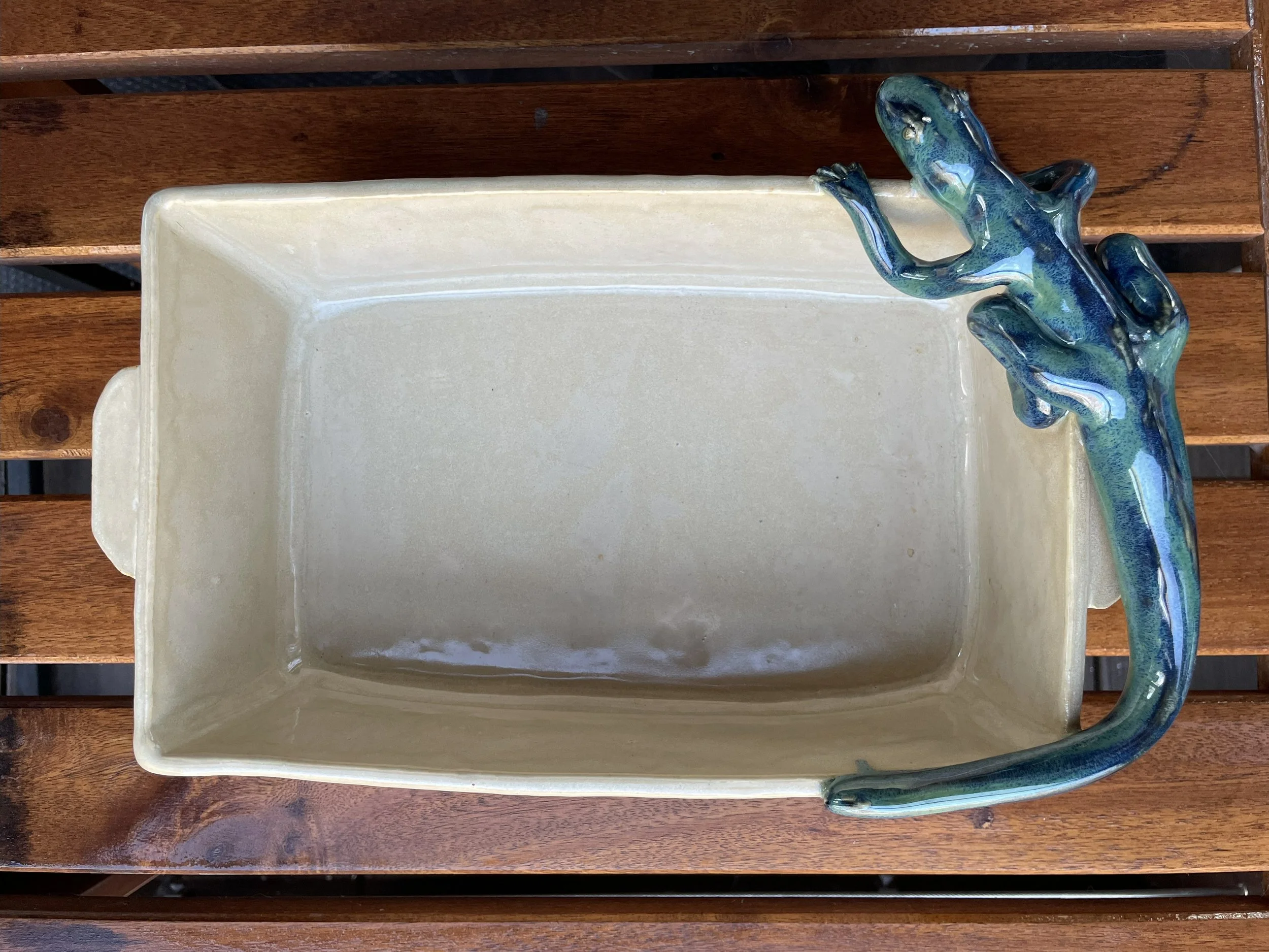 A rectangular ceramic planter with a blue and green lizard sculpture attached to the rim, placed on a wooden surface.