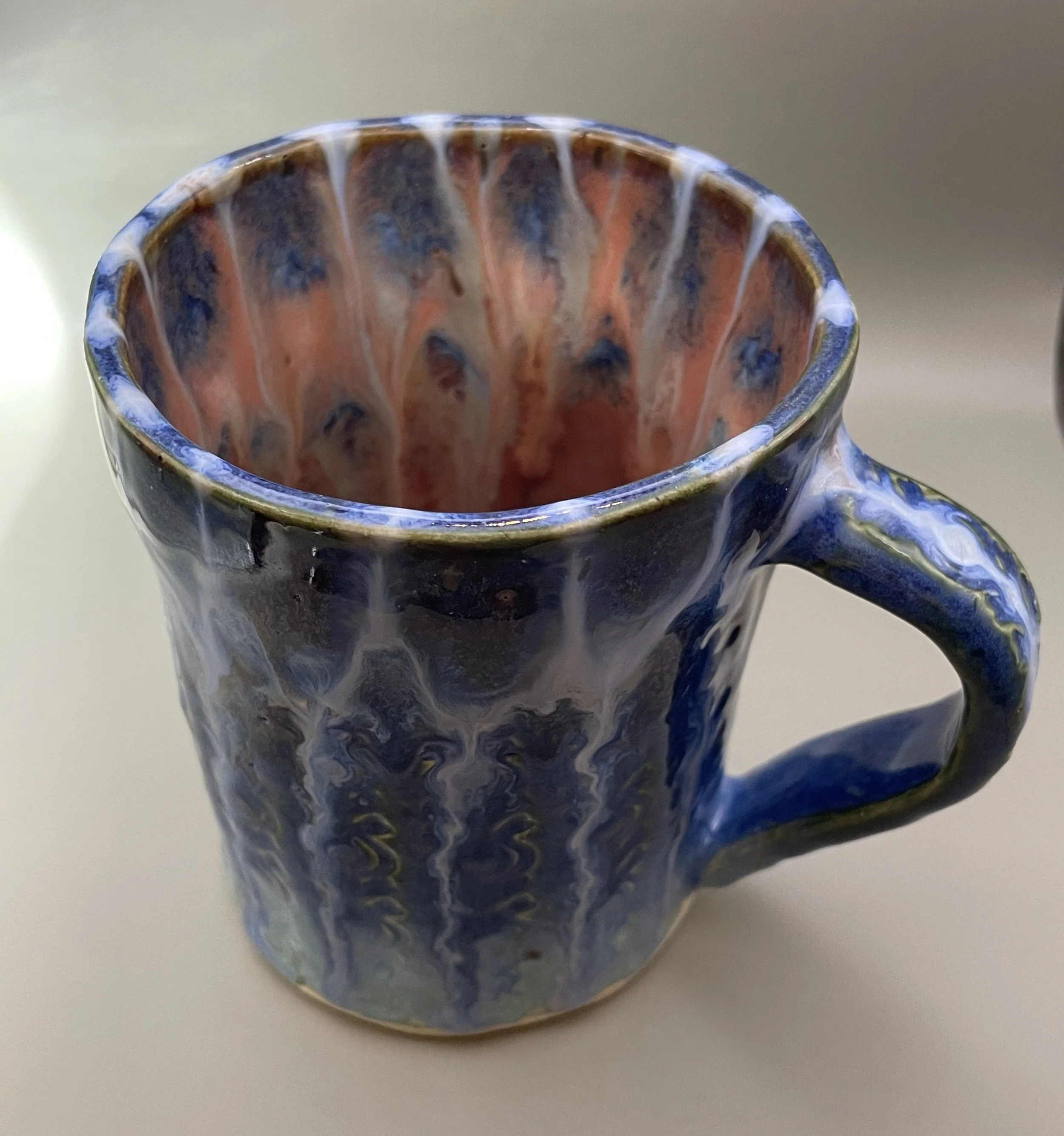 Colorful ceramic mug with blue, orange, and white glaze on a neutral surface.