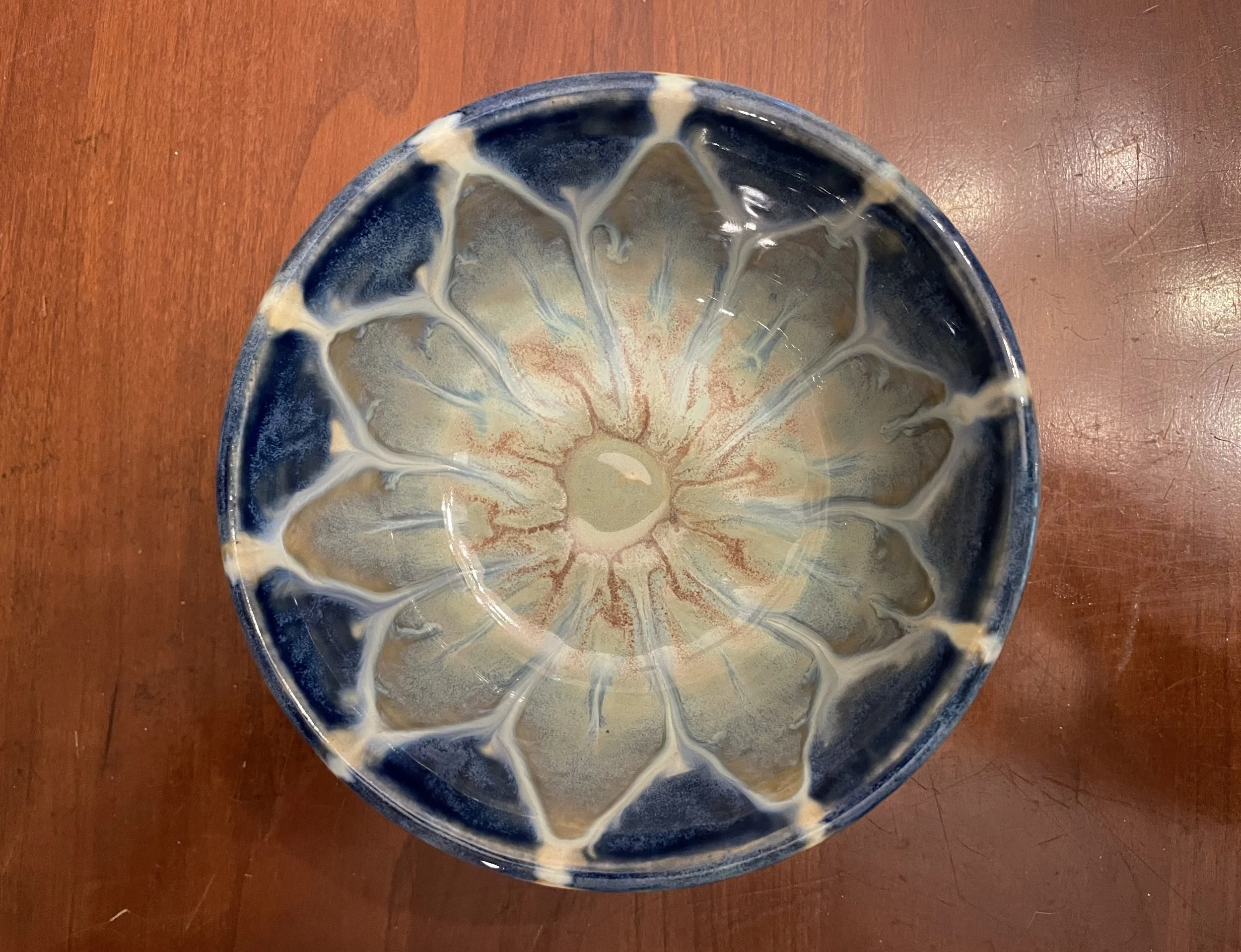 Top-down view of a ceramic bowl with a decorative glaze pattern in shades of blue, beige, and cream on a wooden surface.