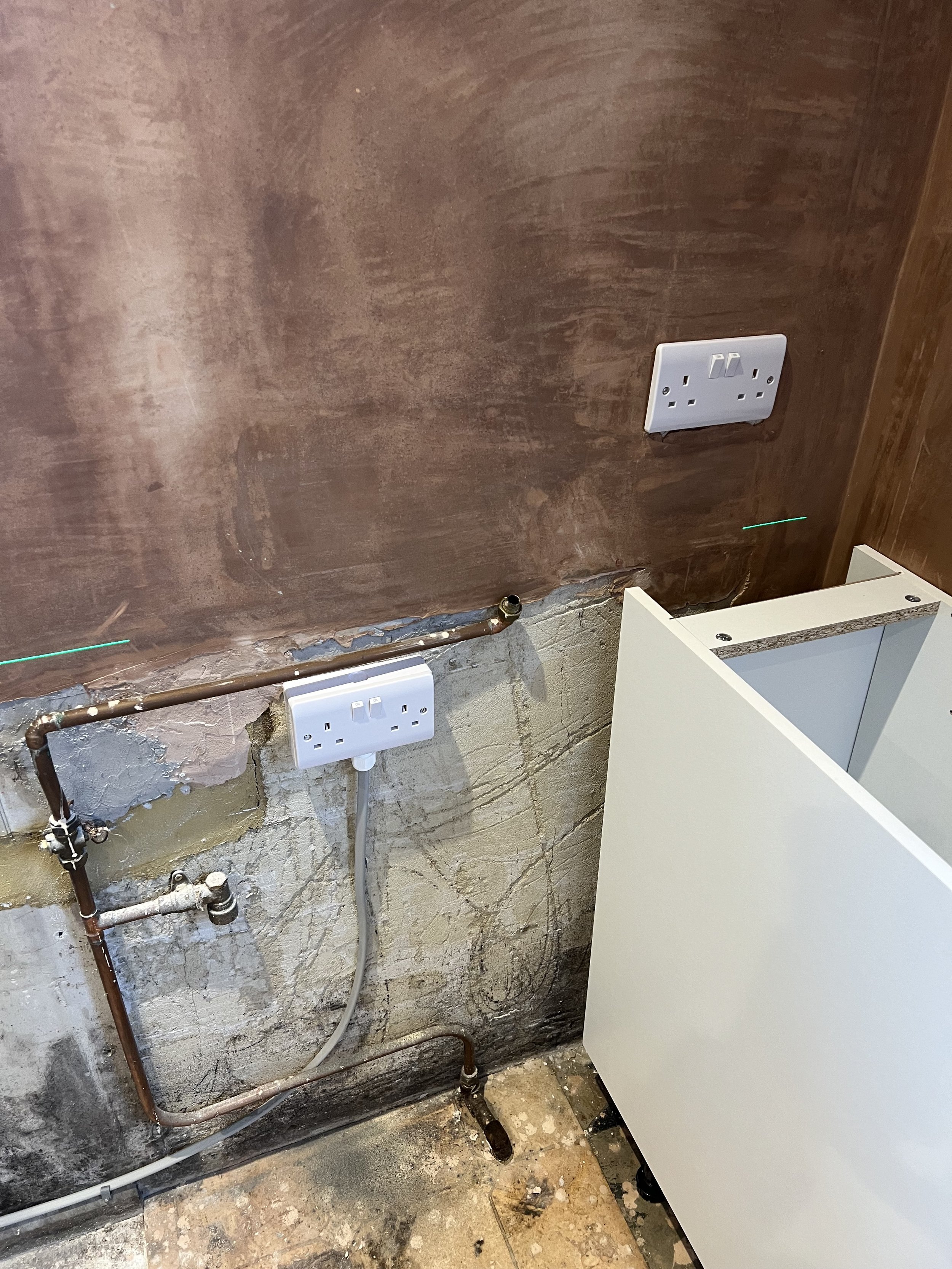 Interior wall with exposed plumbing and electrical outlets, partially prepared for renovation or installation.