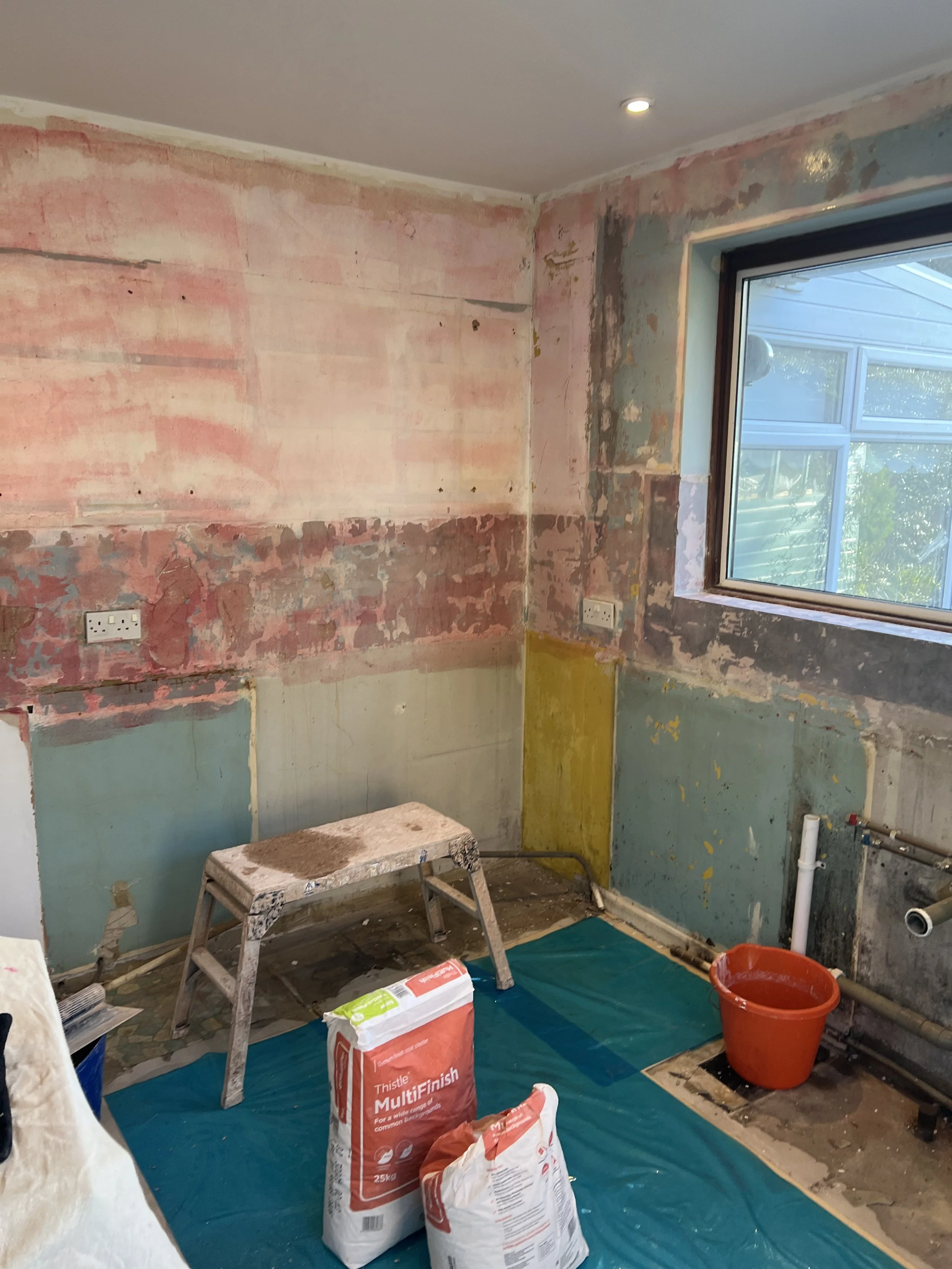 A room under renovation with unfinished walls, a window, painting supplies, and a blue tarp on the floor.