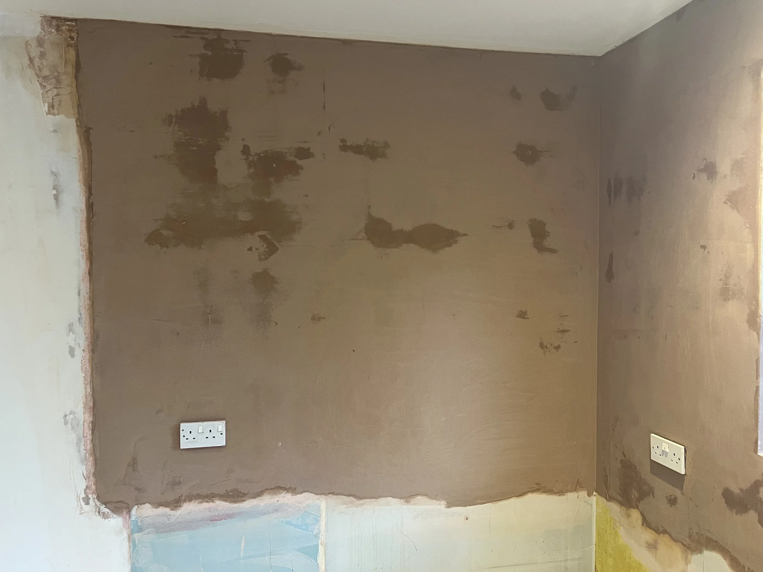 Interior wall undergoing renovation with patches of drywall compound, two electrical outlets, and exposed wall edges.