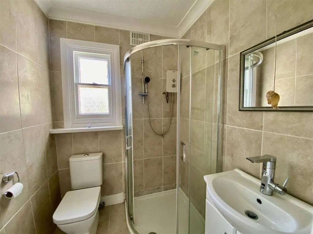 Small bathroom with a window, toilet, corner shower, sink, and mirror.