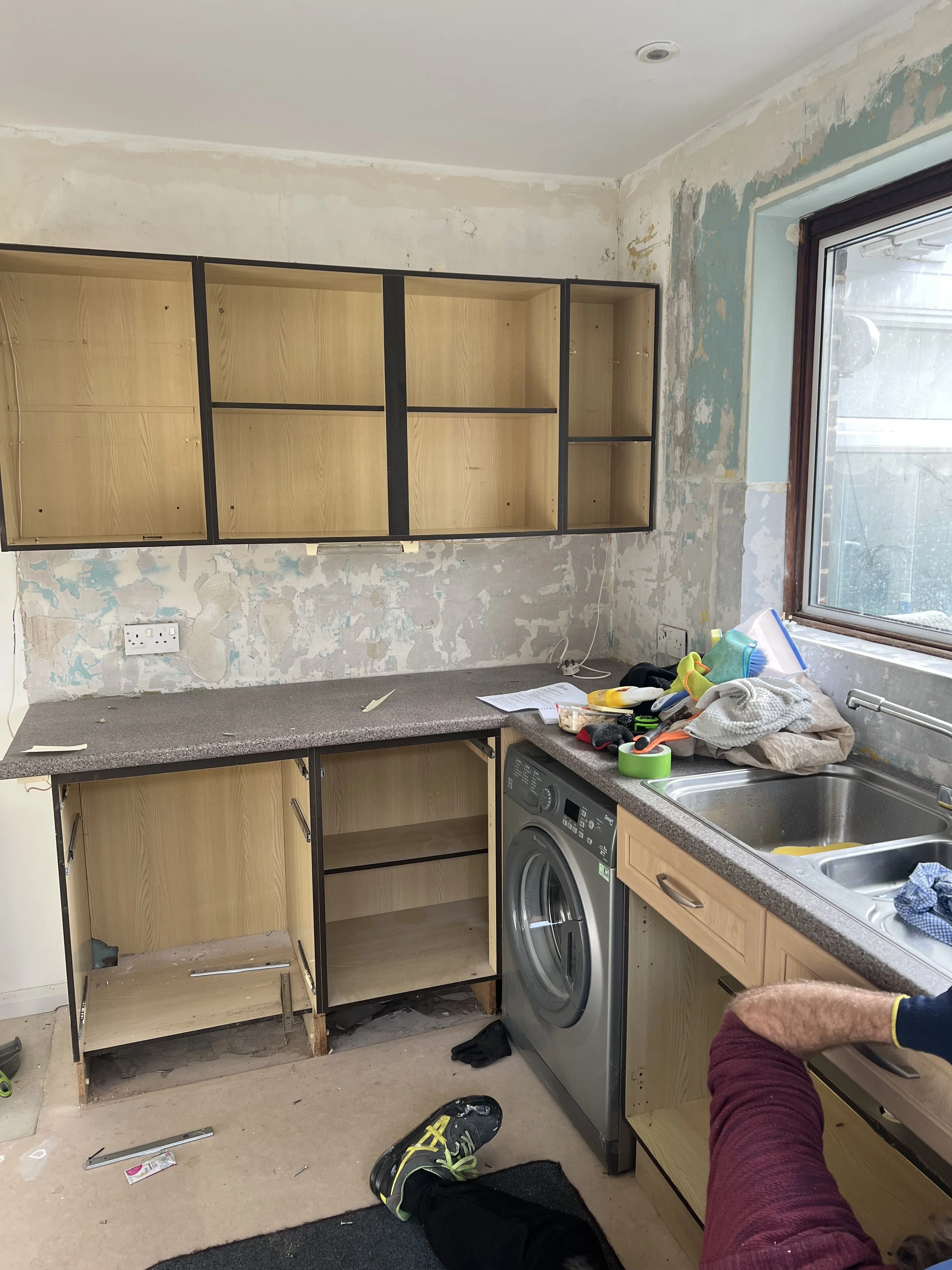 Kitchen under renovation with unfinished cabinets, construction tools, and cleaning supplies scattered on the countertop.