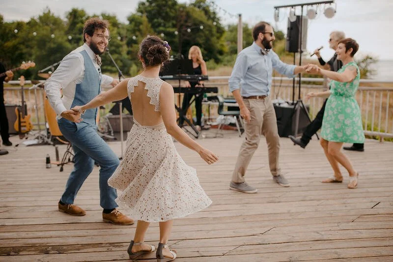 People dancing outdoors on a wooden deck with a band playing in the background.