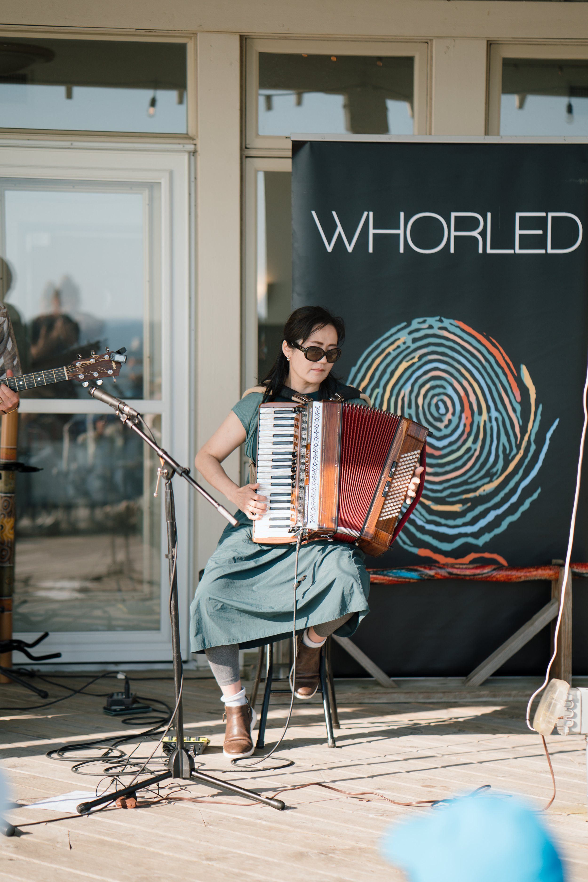 A female musician sitting on a stool playing an accordion on a wooden stage.