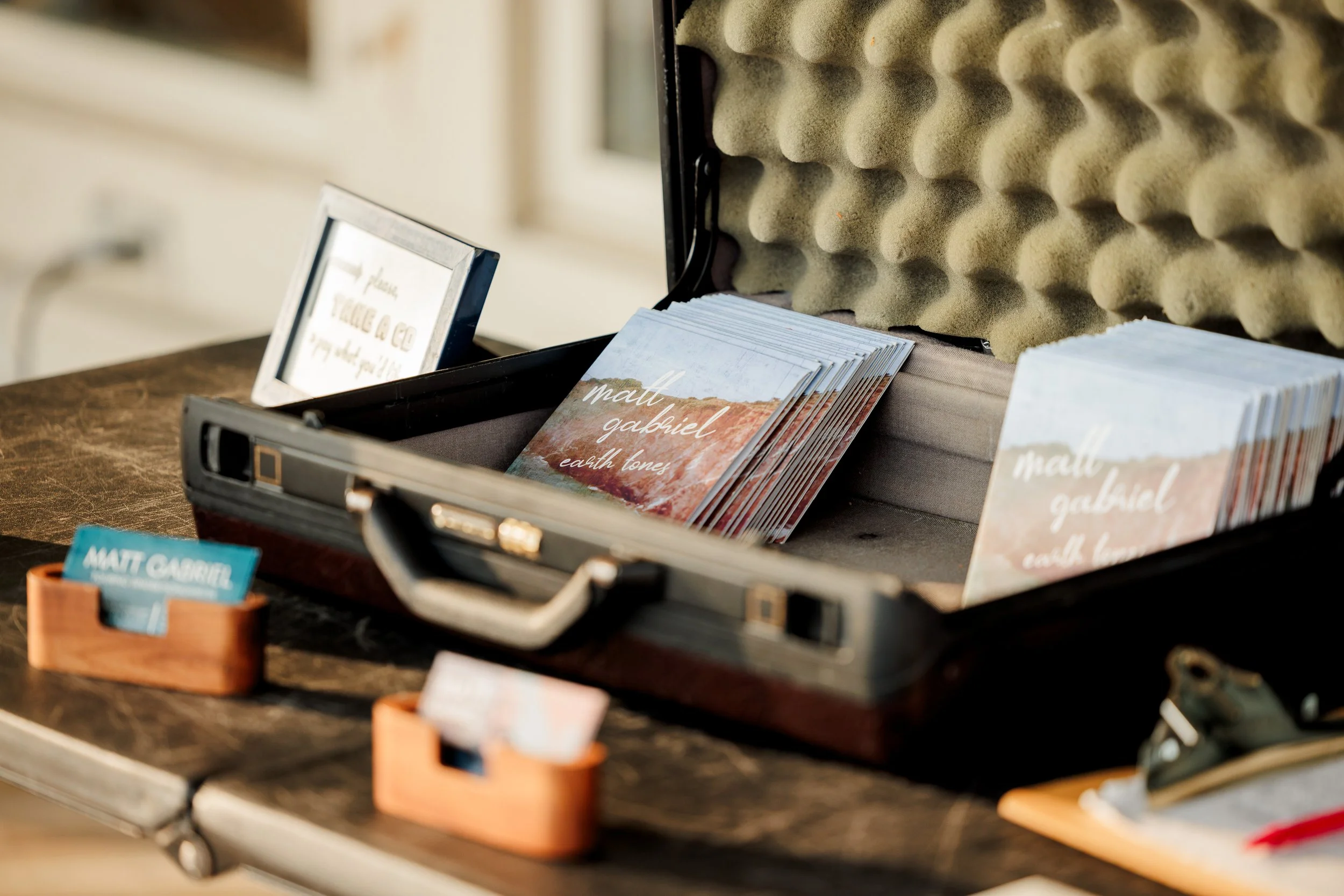 Open briefcase with stacks of business cards for Matt Gabriel on a wooden table, with foam soundproofing on the inside of the briefcase lid.
