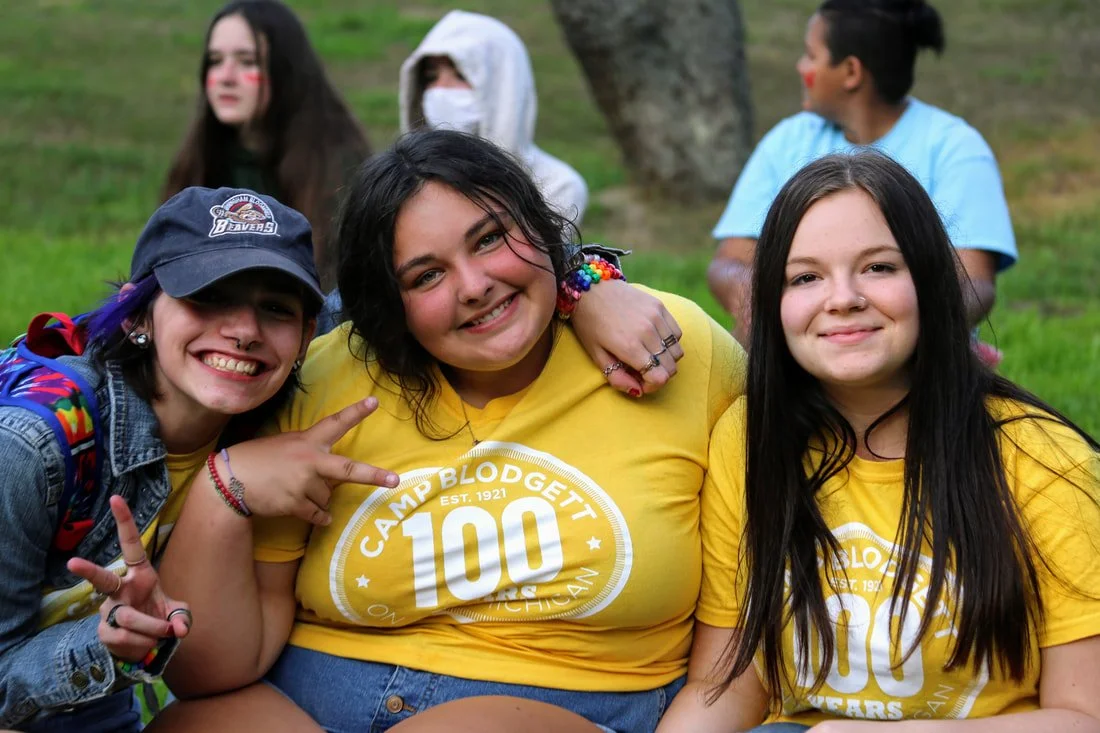 Group of young people smiling, wearing yellow Camp Blodgett t-shirts, outdoors in a park.