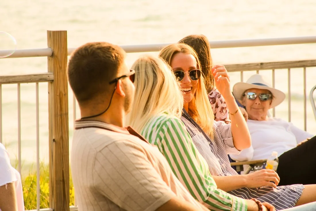 A group of people sitting and chatting outdoors near a body of water during sunset.
