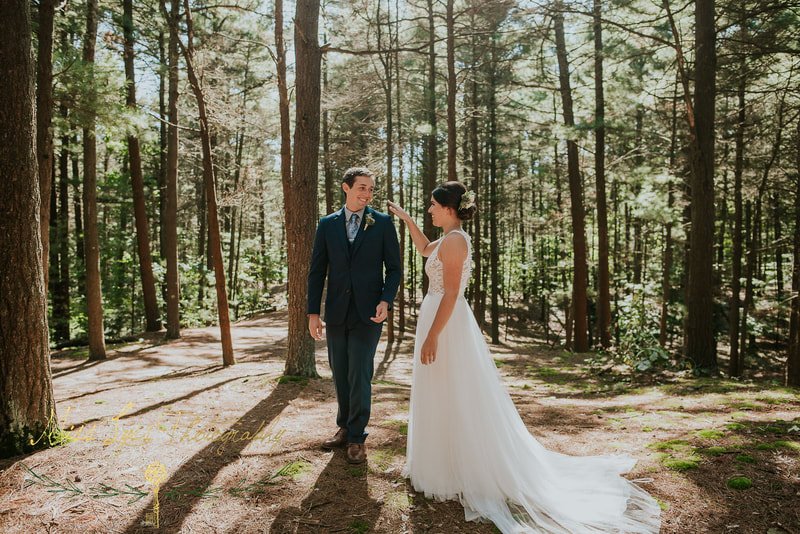 A bride and groom standing in a forest during their wedding, with sunlight filtering through the trees.