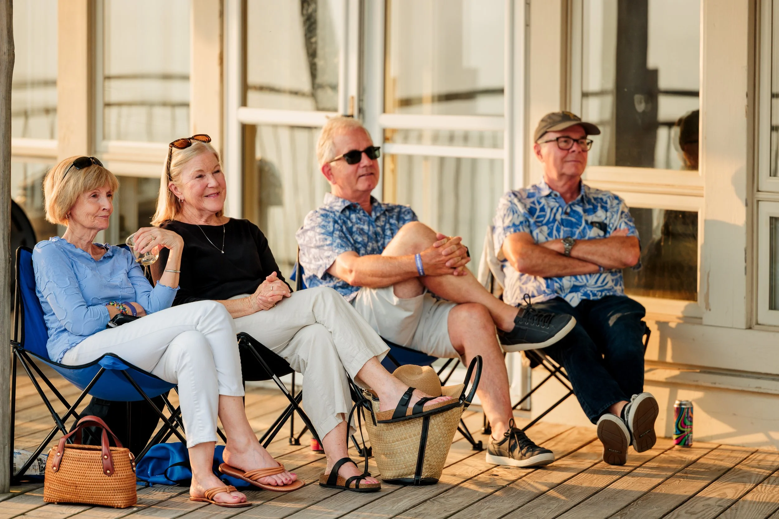 Four older adults sitting on foldable chairs on a wooden deck, relaxing and enjoying a sunset.