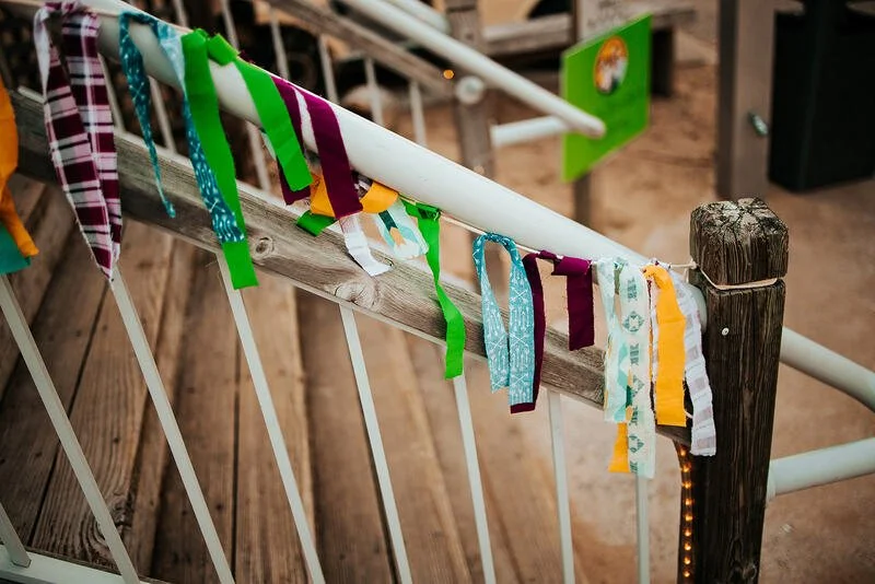 Decorative fabric banners hanging on a white railing outdoors, with wooden flooring and a green sign in the background.