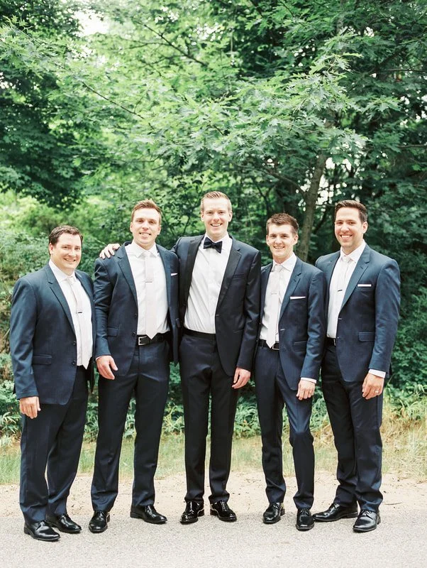 Five men in suits standing outdoors, smiling, with trees in the background.