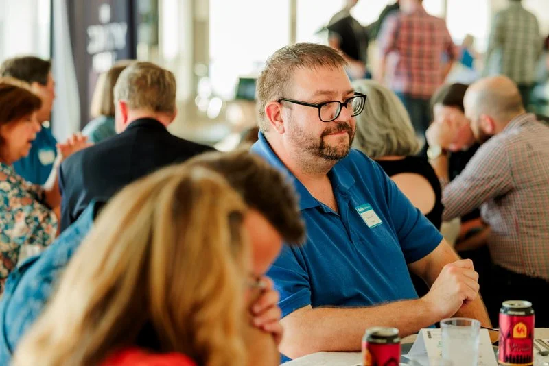 People sitting around a table at a conference or meeting, engaging in conversations.