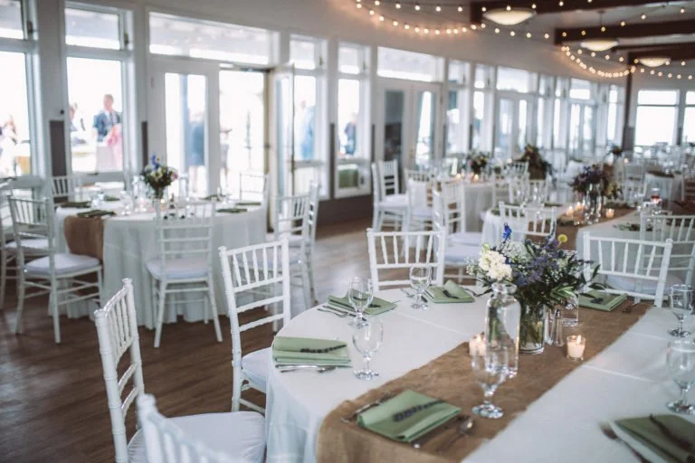 Wedding reception hall with round and rectangular tables decorated with flowers, candles, and green napkins, set for guests.