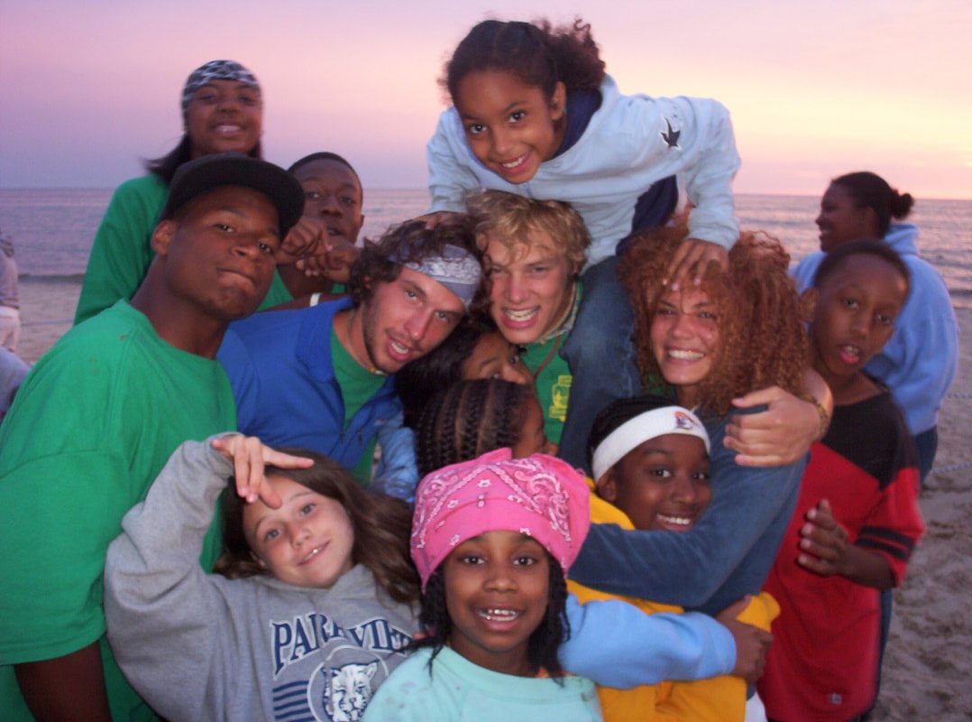 Group of kids and adults at the beach during sunset, smiling and hugging.