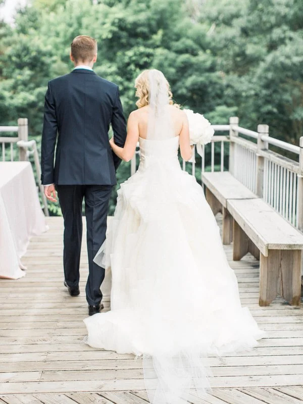Bride and groom walking away on a wooden deck with a forest background during a wedding.