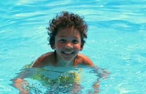 Child swimming in a pool with a big smile.