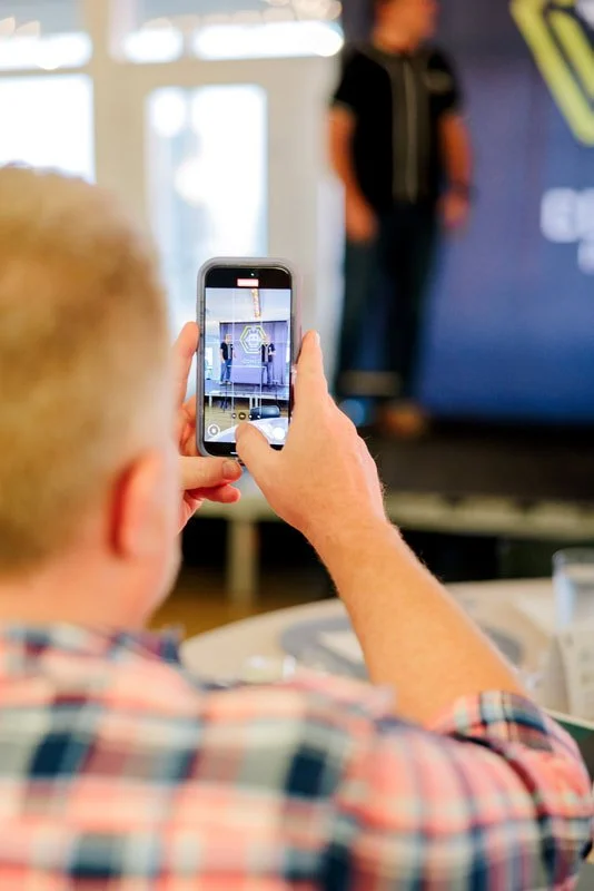 Person taking a photo of a speaker on stage with a smartphone.