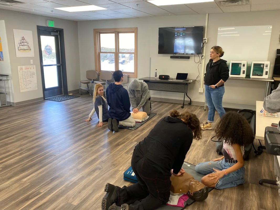 People practicing CPR on mannequins in a classroom setting with an instructor observing.
