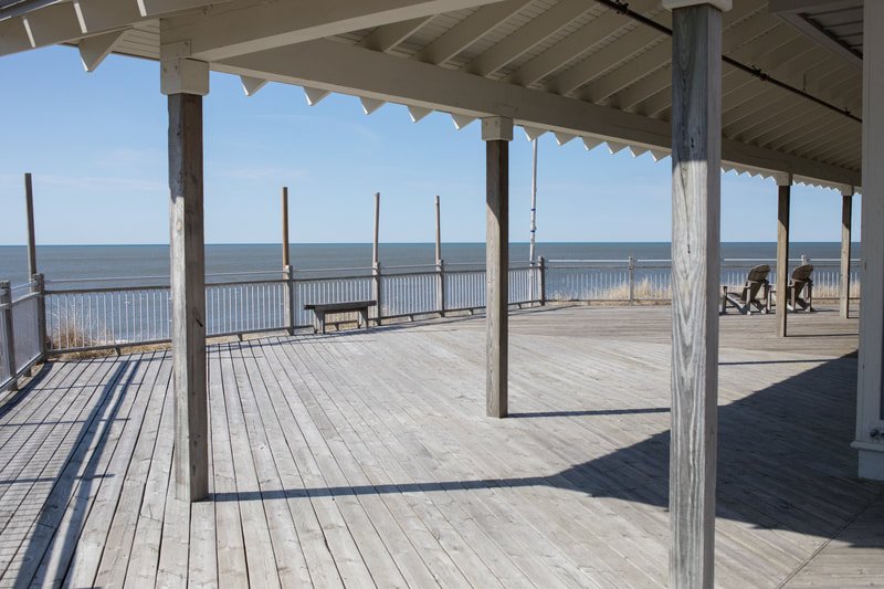 Empty wooden pier or deck overlooking the ocean with benches and railings.
