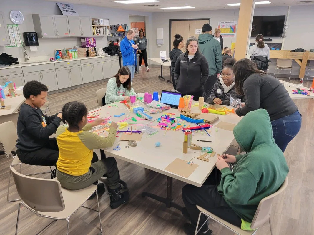 People participating in an arts and crafts workshop around a table with colorful supplies in a classroom or community center.