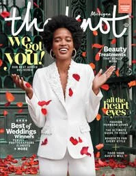 Cover of a magazine featuring a woman with curly hair wearing a white suit with red heart patterns, smiling with open arms.