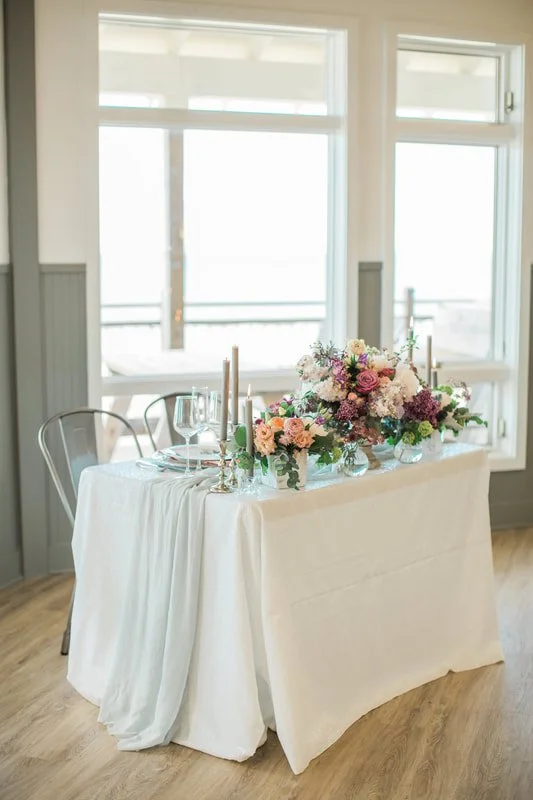 Elegant table setup with floral centerpiece and candles in a bright room with large windows