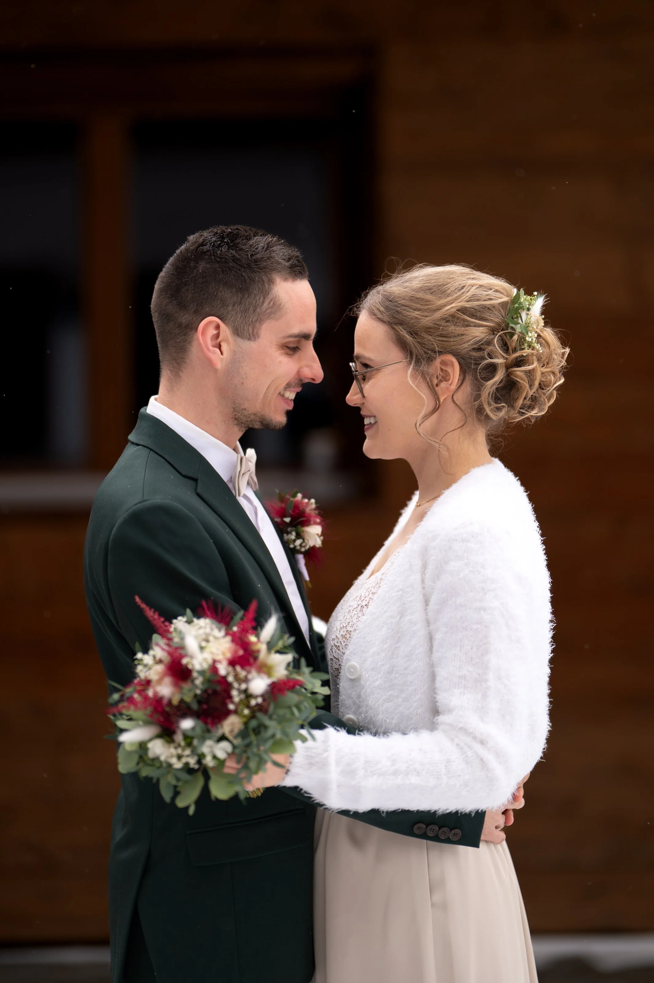 Ein Brautpaar bei einer Hochzeit, sie stehen sich gegenüber, lächeln, und halten sich an den Händen, während die Braut einen Blumenstrauß hält.