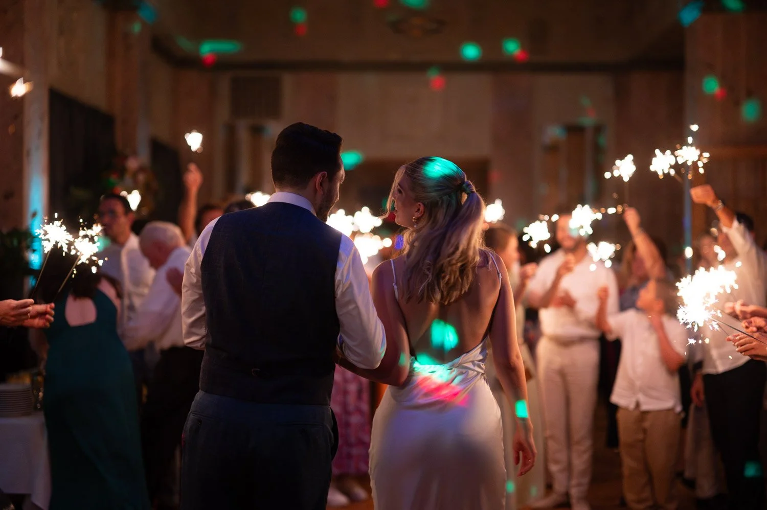 Ein Paar tanzt bei einer Feier, während geschwungene Lichter und Feuerwerkssterne im Hintergrund leuchten.