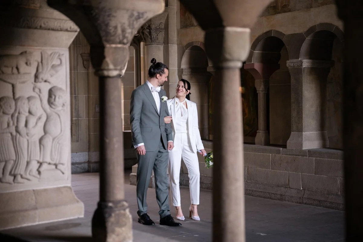 Ein verliebtes Paar in formeller Kleidung bei einer Hochzeit in einem historischen Gebäude mit Steinsäulen.