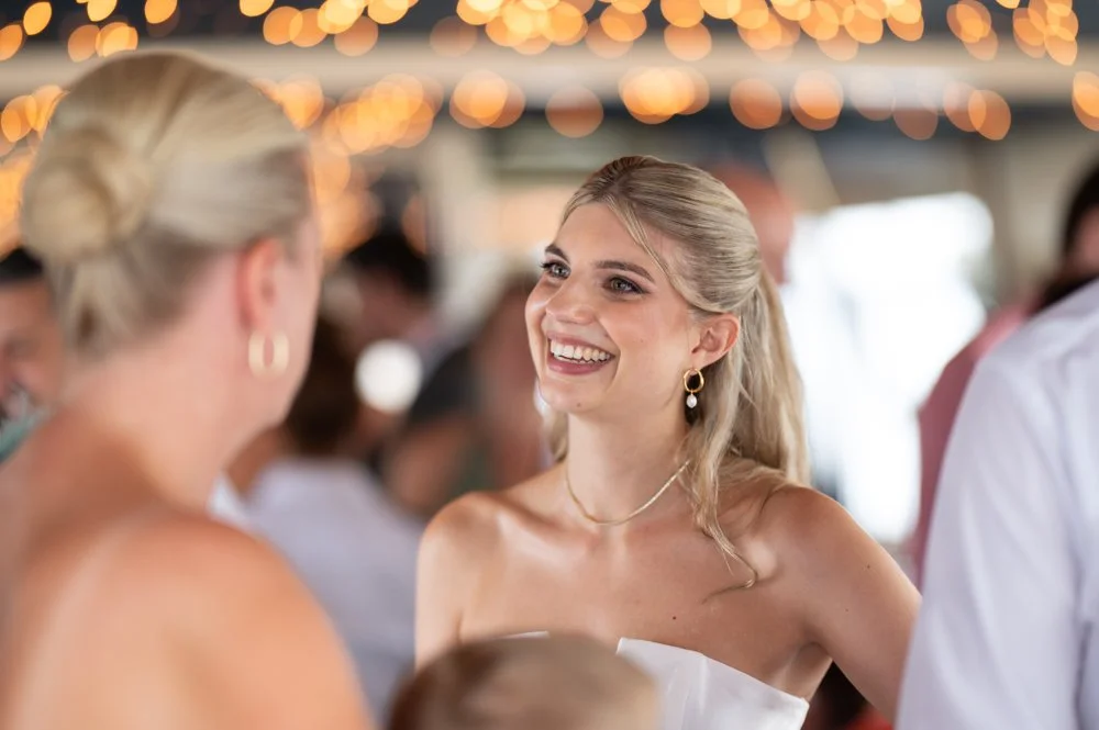 Junge Frau mit blonden Haaren, lachend bei einer Feier, im Hintergrund Lichter und andere Menschen.