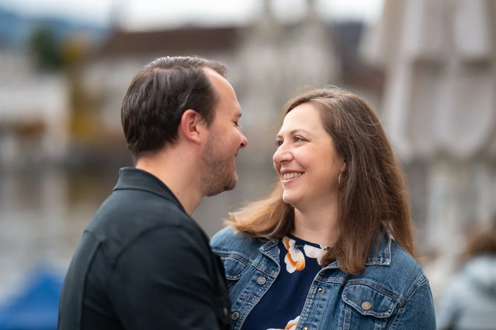 Ein lächelndes Paar blickt sich verliebt an, draußen, vermutlich auf einer Brücke.