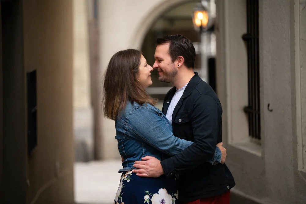 Ein verliebtes Paar in einer engen Gasse, das sich liebevoll anlächelt und umarmt.
