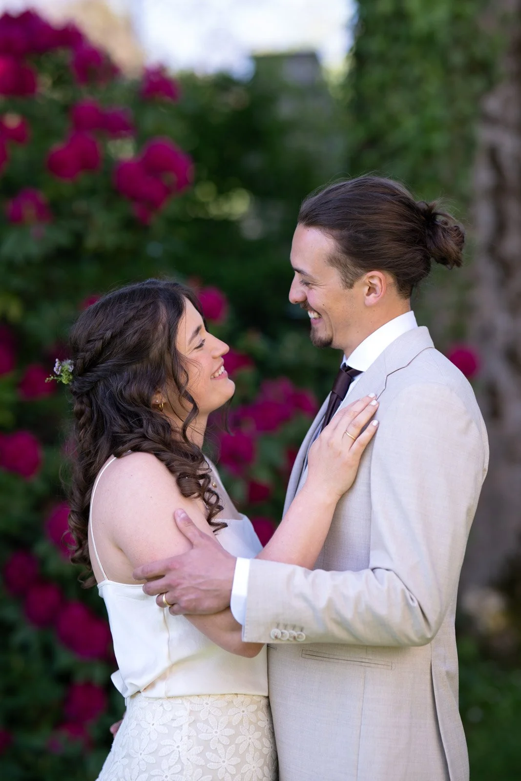 Ein lachendes Paar bei einer Hochzeit im Garten, umgeben von blühenden Rosen.