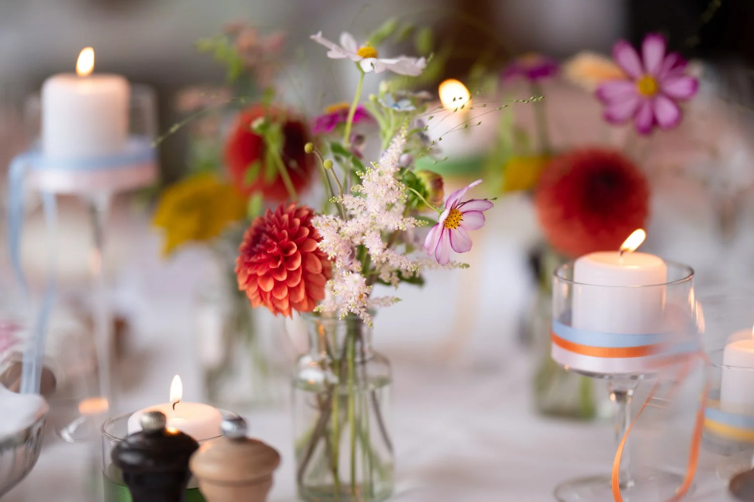 Blumenstrauß in einer Glasvase mit Kerzen umgeben auf einem Tisch bei einer Feier